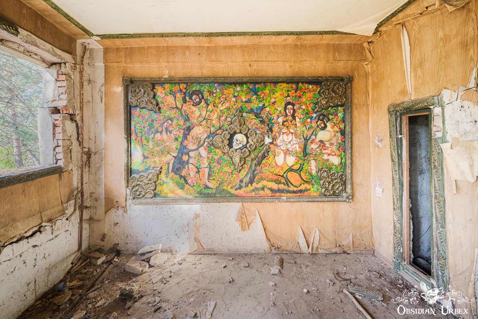 A colorful mural depicting a forest and human figures is painted on the damaged wall of an abandoned, decaying room with peeling paint and debris on the floor.