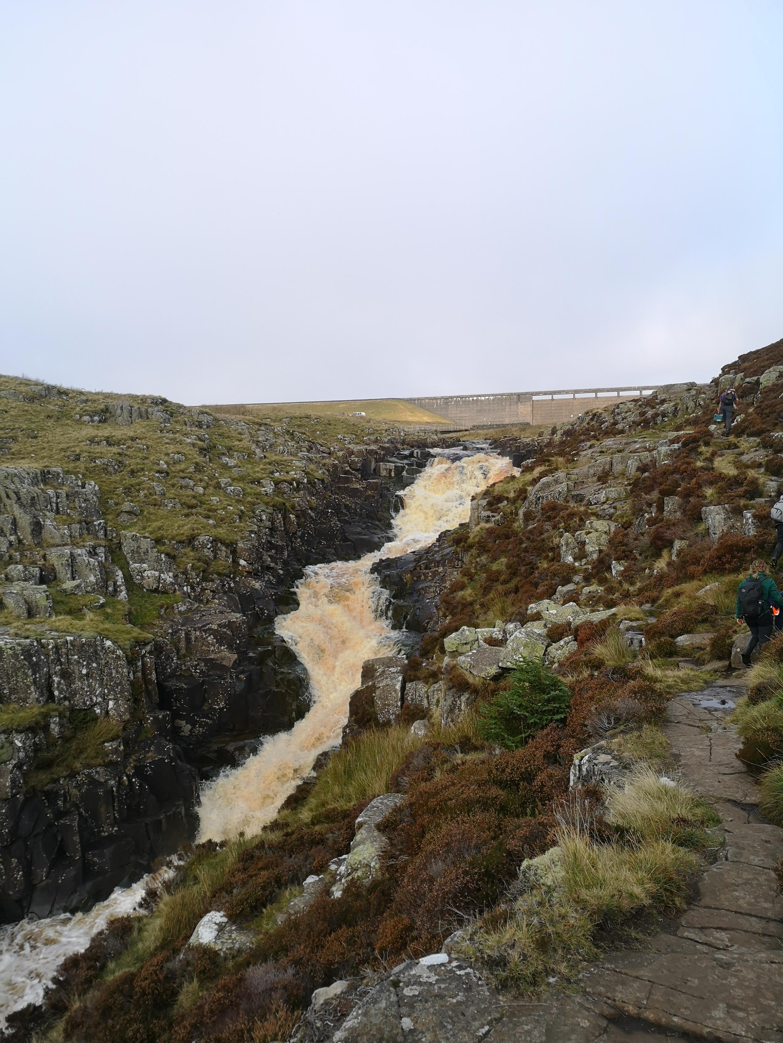 View looking up Cauldron Snout waterfall. A peat coloured brown torrent falling over the hard rock of the Whin Sill in the river Tees, Upper Teesdale. The mist is lifting and Cow Green dam is visible at the top of the photo.
