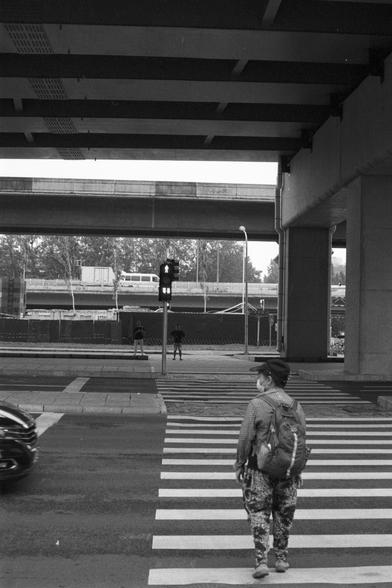 Kentmere Kentmere PAN 400 (FF)

English Alt Text:
A pedestrian stands at a crosswalk, wearing a checkered shirt, patterned pants, and a backpack. The crossing signal is red. A car passes on the left. In the background, multiple elevated roads crisscross above, supported by large concrete pillars. A bus and other vehicles are visible on the upper level. Another pedestrian walks across the street. The image emphasizes urban infrastructure and human movement.

中文替代文字：
一名行人站在人行横道前，身穿格子衬衫、花纹裤子，背着背包。…