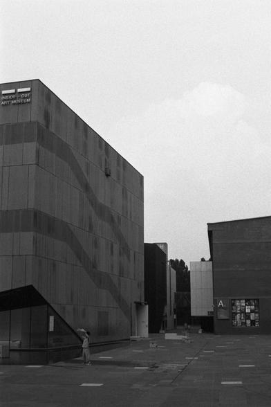 Kentmere Kentmere PAN 400 (FF)

English Alt Text:
Two modern buildings in a public plaza. The left building has a sign reading “INSIDE-OUT ART MUSEUM” and a facade of rectangular panels with a wavy diagonal pattern. A child plays nearby. The right building is simpler, with a bulletin board displaying posters. The ground is paved, and the sky is overcast, adding to the monochrome tone. The scene evokes quiet contemplation in an urban cultural space.

中文替代文字：
公共广场上的两座现代建筑。左侧建筑标有“INSIDE-OUT ART MU…