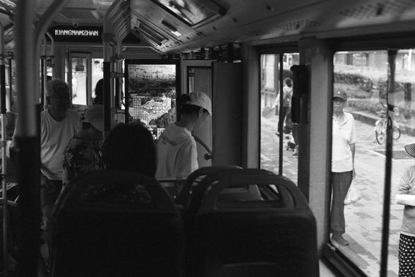 Kentmere Kentmere PAN 400 (FF)

English Alt Text:
Interior of a public bus with passengers seated and standing. Large windows reveal pedestrians outside, including a man peering in and a woman holding a bag. A digital screen displays route information, though partially obscured. Handrails and seats line the bus, which appears stationary. The scene captures a moment of daily urban transit, with quiet interactions between people inside and outside.

中文替代文字：
公交车内部，有乘客坐着和站着。大窗户外可见行人，包括一位向车内张望的男子和一位…