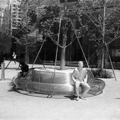 Ilford HP5 Plus 400 (6x6)

English Alt Text:
A modern public art installation in an urban plaza. A circular bench made of metal tubes surrounds a tree. Suspended cables support the tree from a circular frame above. Integrated into the bench is a life-sized metallic statue of a seated human figure, blending seamlessly with the structure. Surrounding the installation are glass-covered buildings, pedestrians, and similarly supported trees. The design merges functionality, sculpture, and nature in …