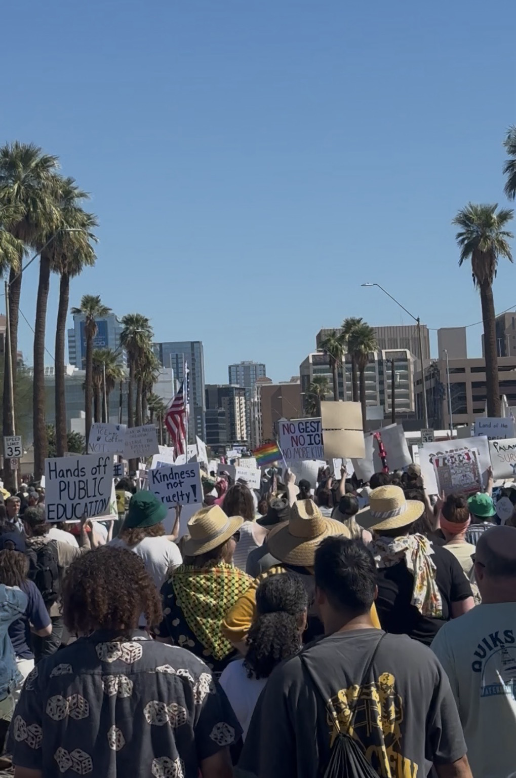 Crowd of people marching away from the camera down a street, many holding signs or flags