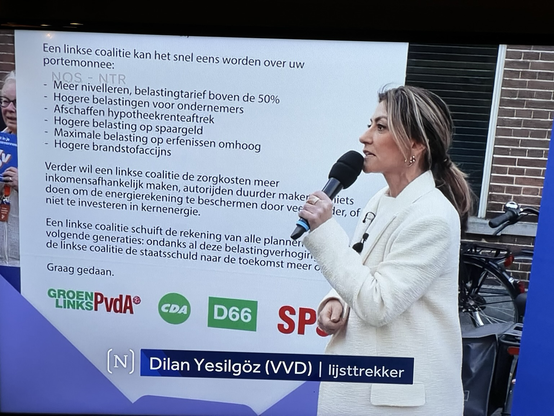 Yesilgoz met microfoon in de hand voor een bord met wat voor verschrikkelijke dingen ‘links’ allemaal wil (GL-PvdA, CDA, D66, SP)