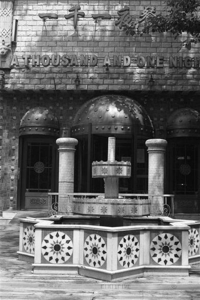 Kentmere Kentmere PAN 400 (FF)

English Alt Text:
A black-and-white photo of a building with Middle Eastern-inspired architecture. The sign reads “A THOUSAND AND ONE NIGHTS.” The facade features domed doorways and square tiles with geometric patterns. In front stands an octagonal fountain with star-shaped designs and a central column with water spouts. The scene evokes the fantasy and cultural richness of the Arabian Nights tales, blending storytelling themes with decorative architecture.

中文替代…