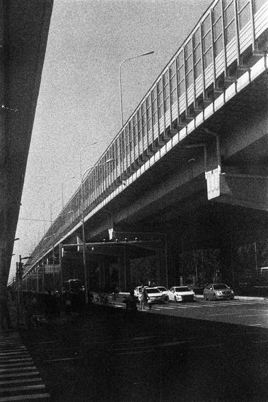 ORWO P400 (FF)

English Alt Text:
A black-and-white photograph captures a multi-level highway structure. The upper roadway is supported by massive concrete pillars and lined with streetlights. Below, cars and buses move along the lower road, indicating active traffic. The image is grainy, emphasizing its documentary or vintage aesthetic. Strong lines from the highway and pillars guide the viewer’s eye into the distance, creating a sense of scale and urban infrastructure.

中文替代文本：
这是一张黑白照片，展示了一个…