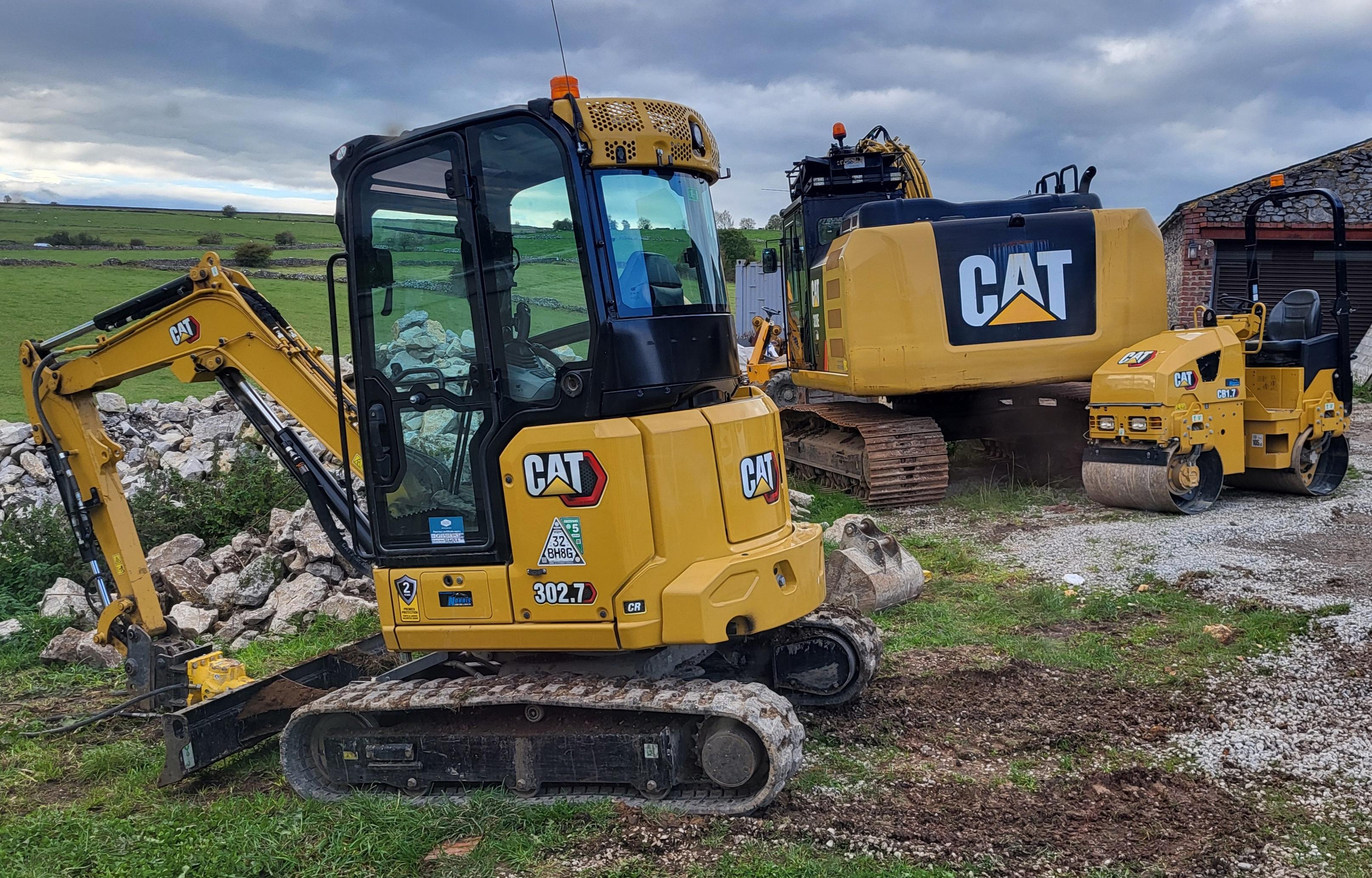 Three peices of yellow cat branded machinery on grass/rock