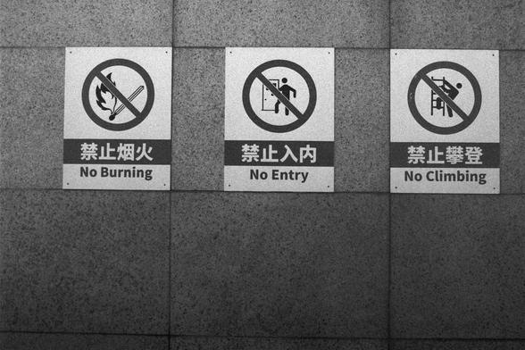 Ilford HP5 Plus 400 (FF)

English Alt Text:
Three safety signs mounted on a tiled wall. Each sign features a red prohibition symbol and bilingual text in Chinese and English. From left to right: “No Burning” with a flame and matchstick icon; “No Entry” with a person walking through a doorway; and “No Climbing” with a person climbing a ladder. The signs are clear and bold, designed to prevent fire hazards, unauthorized access, and unsafe climbing in a restricted area.

中文替代文本：
三块安全警示牌安装在瓷砖墙上。每块牌…