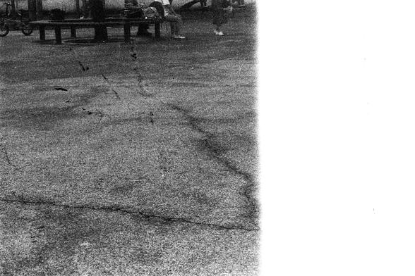 ORWO P400 (FF)

English Alt Text: A grayscale photo of an outdoor urban space. In the foreground, a cracked paved surface leads to a bench under a tree. Several people are gathered—some sitting, others standing—engaged in quiet conversation or observation. The tree provides shade, and its trunk is partially visible. The right side of the image is overexposed, making details in that area hard to distinguish. The overall tone is subdued and nostalgic, with a vintage feel due to the black-and-whit…