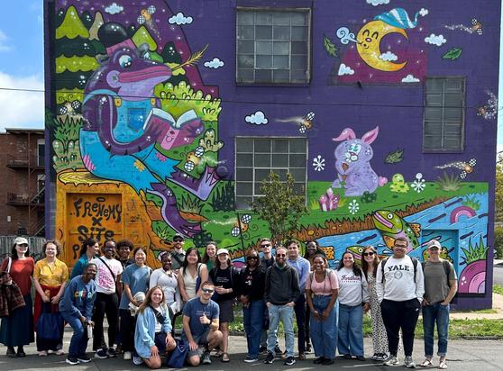 A group of people in front of a colorful mural on a building. 