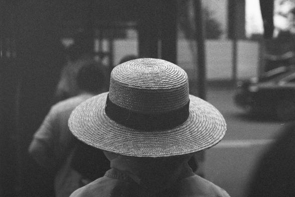 Ilford HP5 Plus 400 (FF)

English Alt Text:
A black-and-white photo showing the back of a person wearing a wide-brimmed straw hat with a dark band. The person stands in an urban setting, possibly near a bus stop or sidewalk. Other people and a vehicle are faintly visible in the background. The focus is on the hat and shoulders, evoking a nostalgic or vintage mood. The hat’s traditional style contrasts with the modern urban environment, creating a timeless feel.

中文替代文字：
一张黑白照片，画面聚焦在一位戴着宽檐草帽的人背影…