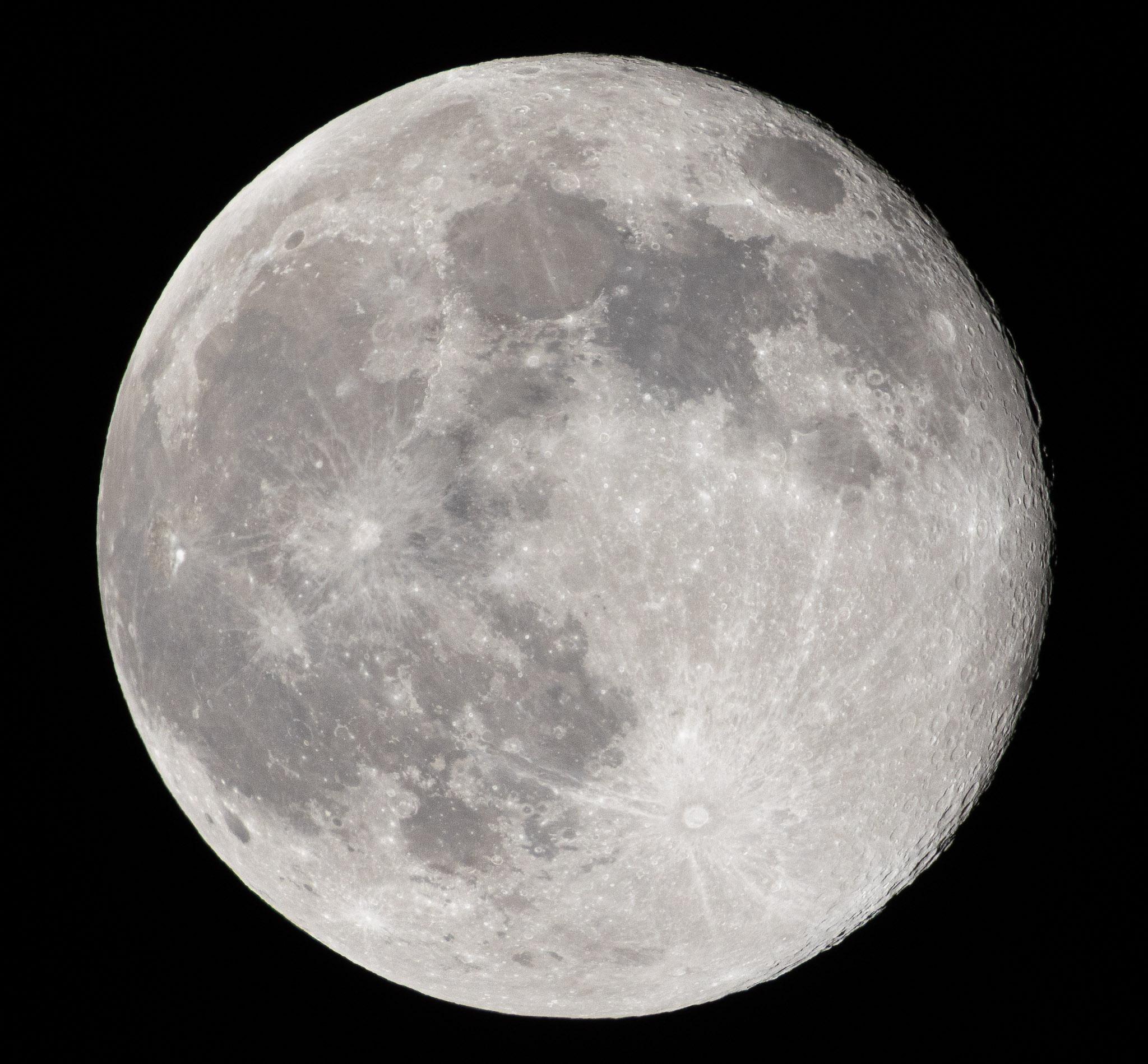 A crisp photo of the full moon, with just a fringe of shadow on the right edge showing crater rims in relief.