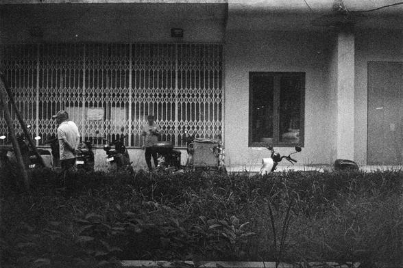 Shanghai GP3 400 PAN (FF)

English Alt Text: A grainy black-and-white photo of a building with a metal accordion-style gate. Several motorbikes are parked in front. Two people are visible: one standing on the left wearing a cap and light shirt, and another near the center interacting with a motorbike. The foreground is filled with overgrown grass and weeds, contrasting with the structured building. The image feels candid and slightly nostalgic.

中文替代文本： 这是一张颗粒感强烈的黑白照片，拍摄的是一栋建筑，建筑前有金属折叠门。门前停着几辆摩…