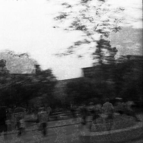 Ilford HP5 Plus 400 (6x6)

English Alt Text: A black-and-white photo of an urban outdoor setting, possibly a park or plaza. The image is heavily blurred due to camera movement, creating a sense of motion and distortion. Several people are visible but indistinct, appearing as ghostly figures. Trees and buildings form the backdrop, though their details are obscured. The photo has a textured overlay, possibly from aged film or print damage, adding a vintage and abstract quality. The overall effect…