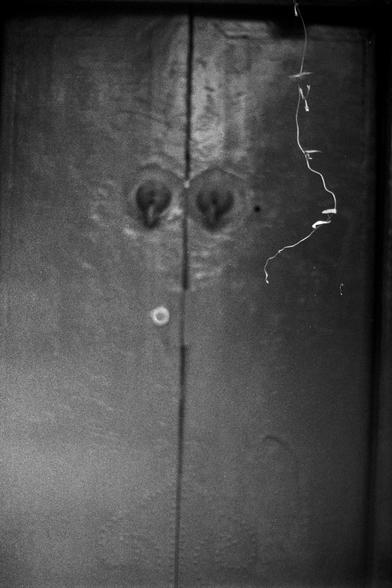 Fujifilm NEOPAN SS (FF)

English Alt Text: A black-and-white close-up of two aged wooden doors with a vertical seam where they meet. Near the top center are two symmetrical, teardrop-shaped metal fixtures. A thin, curly string or vine hangs from the top right, adding contrast to the textured wood. The image evokes a moody, artistic atmosphere.

中文替代文字：
这是一张黑白特写照片，展示两扇老旧木门，中间有垂直缝隙。门的上方中央有两个对称的水滴形金属装饰。右上角垂下一根细长弯曲的线或藤蔓，与木门的粗糙质感形成对比。整体画面具有艺术感和沉静氛围。