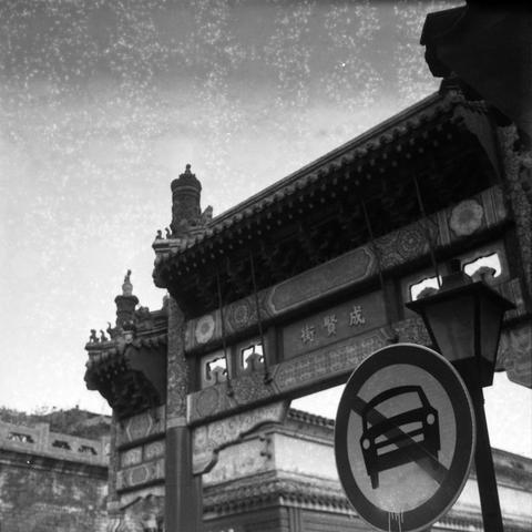 Ilford HP5 Plus 400 (6x6)
English Alt Text
A black-and-white photo of a traditional Chinese gate with ornate carvings and layered roof tiles. The gate bears the characters “成贤街” (Chengxian Street), indicating a culturally significant location. The structure is symmetrical, with decorative beams and eaves typical of classical Chinese architecture. In front of the gate, a modern traffic sign shows a crossed-out car symbol, indicating that cars are prohibited. The juxtaposition of ancient design a…