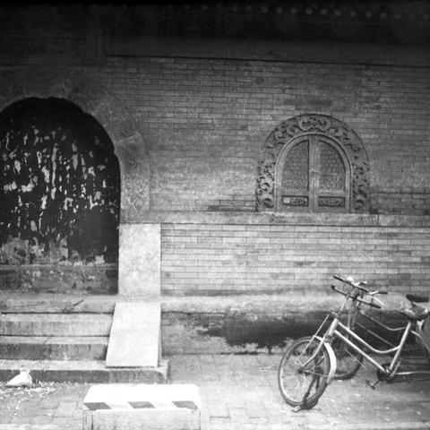 Ilford HP5 Plus 400 (6x6)

English Alt Text
A black-and-white photo of an old brick wall featuring an arched doorway and a decorative window. The doorway is worn and partially damaged, while the window has ornate carvings. Stone steps lead up to the entrance. A bicycle leans against the wall to the right, adding a modern contrast. A striped concrete block sits in the foreground. The scene blends historical architecture with everyday urban life, evoking a sense of quiet nostalgia.

中文图像替代文字
这是一张…