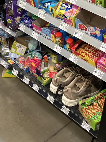 A retail shelf featuring various candies and toys alongside a pair of beige sneakers.