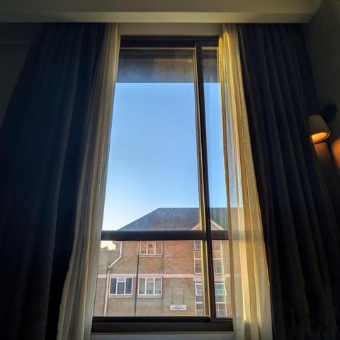 Looking through a modern window thirty-four minutes after sunrise, there is a generic brick house with a black roof beneath a clear blue cloudless sky.