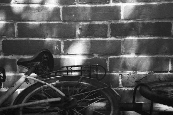 Ilford HP5 Plus 400 (FF)

English Alt Text: A black and white close-up of two bicycles partially visible in front of a brick wall. One bicycle’s seat and rear wheel dominate the foreground, while the second bicycle’s front wheel and frame peek in from the right. The brick wall is textured and bathed in soft light and shadow. The image conveys a quiet urban scene with a vintage, contemplative mood.

中文替代文字：
这是一张黑白特写照片，两辆自行车部分出现在砖墙前。一辆自行车的座椅和后轮位于画面前景，另一辆的前轮和车架从右侧探出。砖墙表面有丰富的纹理，光影柔和。画面传达出一种宁静的城市氛围，…