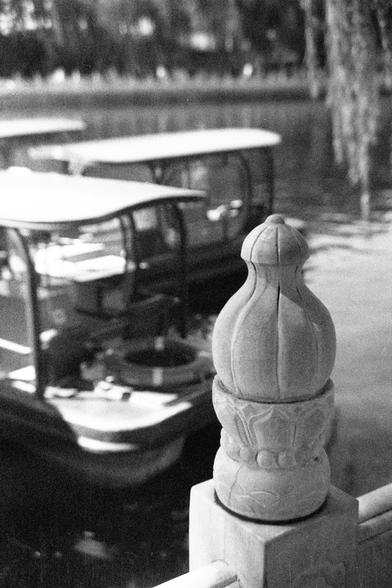 Ilford HP5 Plus 400 (FF)


English Alt Text:
A black-and-white close-up photo of a carved stone or concrete post, possibly part of a railing. The post features ornate detailing and a bulbous top resembling a lotus bud. In the blurred background, covered leisure boats are docked on calm water, with reflections shimmering on the surface. The composition emphasizes the craftsmanship of the post while evoking a peaceful, waterside atmosphere.

中文替代文字：
这是一张黑白特写照片，展示了一个雕刻精美的石柱或混凝土柱，可能是栏杆的一部分。柱顶呈莲花状，装…