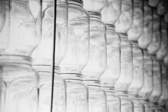 Ilford HP5 Plus 400 (FF)

English Alt Text: A black and white image displays a close-up view of multiple transparent glass jars arranged in neat rows and columns. The jars are identical in shape and size, creating a symmetrical and repetitive pattern. Reflections and shadows on the glass surfaces add depth and texture, while the monochrome palette emphasizes form over color. The composition has an abstract quality, inviting viewers to focus on geometry, light play, and the subtle variations in …