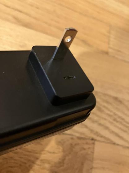 Close-up of a black electrical plug with only a single prong. The other prong has broken off and is missing.