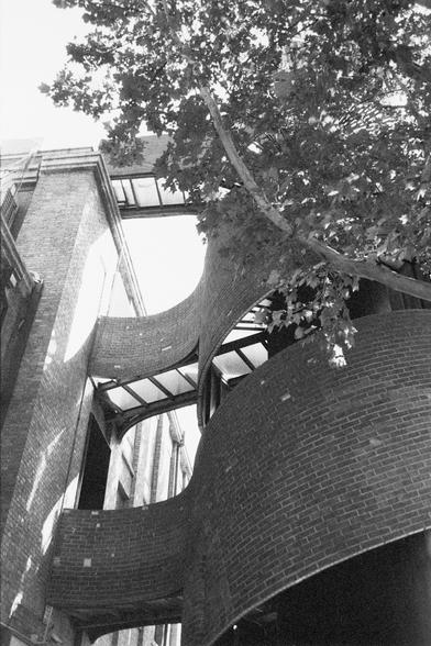 Ilford HP5 Plus 400 (FF)

English Alt Text: A modern architectural installation featuring curved brick walls and metal framework is integrated into an older brick building. The design includes wave-like forms that contrast with the straight lines of the surrounding traditional architecture. A tree with dense foliage partially obscures the view, adding a natural element. Light and shadow play across the textured surfaces, highlighting the innovative use of materials and shapes. The scene evokes …