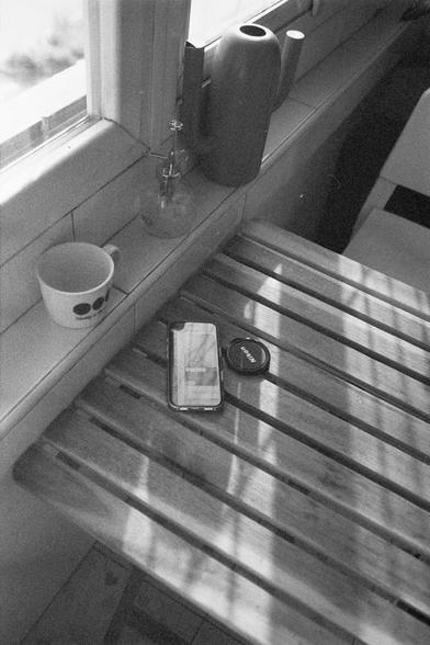 Ilford HP5 Plus 400 (FF)

English Alt Text: A cozy black-and-white photo of a windowsill scene. A white mug with a face design, a glass spray bottle, and a cactus-shaped watering can sit on the sill. Below is a wooden slatted table holding a smartphone and a Nikon lens cap. The phone screen shows a login interface with “Log In” and “Sign Up” buttons. Sunlight casts soft shadows across the table.

中文替代文字： 这是一张温馨的黑白照片，描绘了窗台上的一幕。窗台上放着一个带有脸部图案的白色杯子、一瓶玻璃喷雾器和一个仙人掌形状的浇水壶。下方是一个木质条纹桌面，桌上有一部智能手机和一个尼康镜头盖。…