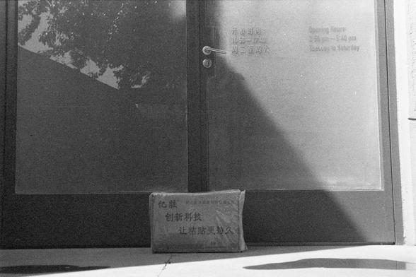 Ilford HP5 Plus 400 (FF)

English Alt Text: A monochrome photo of a glass door with a metal handle and lock. A small package rests on the ground in front of the door. Business hours are printed in both Chinese and English on the glass: “Opening Hours 9:30 am - 5:40 pm, Tuesday to Saturday.” Reflections of trees are visible in the glass. The package has Chinese text promoting adhesive technology.

中文替代文字： 这是一张黑白照片，展示了一扇带金属把手和锁的玻璃门。门前地上放着一个小包裹。玻璃上印有中英文营业时间：“开放时间 9:30 - 17:40，周二至周六。”玻璃上可见树木的倒影。包裹上…