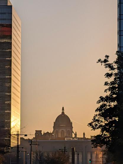 A domed building is framed by two tall structures and silhouetted trees under a warm, glowing sky.