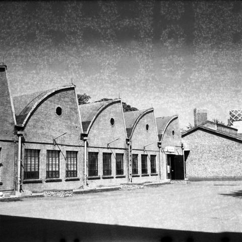 Ilford HP5 Plus 400 (6x6)

English Alt Text: A black-and-white photograph of a row of industrial buildings with curved roofs. The architecture features large rectangular windows and circular ventilation openings near the roof peaks. The buildings are made of brick and have a utilitarian design typical of early to mid-20th century factories or warehouses. The image has a historical feel, highlighting the symmetry and functional aesthetics of industrial architecture.

中文替代文字：
这是一张黑白照片，展示了一排屋顶弯曲的工…