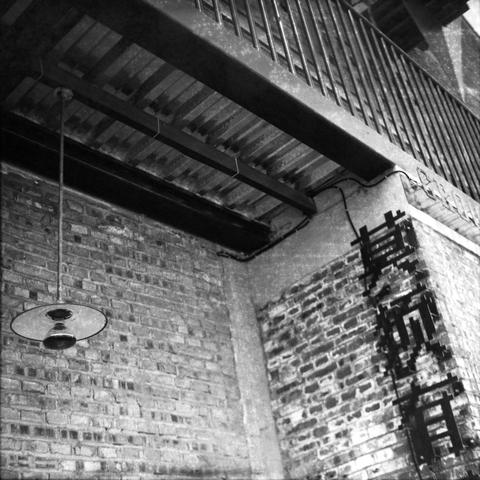 Ilford HP5 Plus 400 (6x6)

English Alt Text: A gritty black and white photo shows an urban scene with a brick wall, an industrial-style hanging light, and a metal ceiling structure with beams. A balcony with vertical railings is visible above. On the right side of the wall, Chinese characters read “Non-existent” adding a personal or rebellious tone. The image blends industrial architecture with expressive street art.

中文替代文字： 这是一张黑白照片，画面呈现都市风格：砖墙、工业风吊灯和带有横梁的金属天花板结构。上方可见带有垂直栏杆的阳台。墙右侧写有中文“莫须有”，传达…