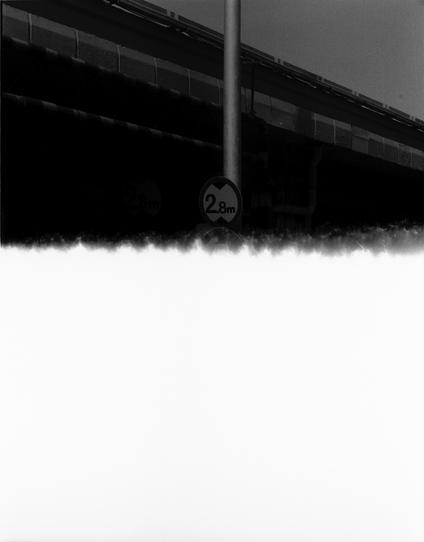 Ilford Pan 100 (FF)

English Alt Text:
A partially obscured urban scene showing the upper portion of a road or railway overpass. A height restriction sign reading “2.8m” is mounted on a pole in front of the overpass structure. The sign is circular with a bold border, indicating maximum vehicle height. The overpass is made of concrete and steel, with visible support beams. The lower half of the image is covered by a white, jagged-edged area, possibly due to overexposure or image damage. The visi…