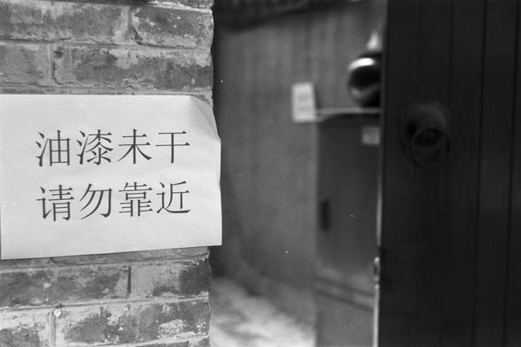 Ilford Pan 100 (FF)

English Alt Text: A black-and-white photo of a brick wall with a paper sign attached. The sign, written in Chinese, reads “Paint not dry. Please do not approach.” It’s placed near a doorway, with part of the interior visible, including a large container. The scene suggests a cautionary moment in a residential or public space, with the sign warning passersby to avoid contact with freshly painted surfaces.

中文替代文字：
这是一张黑白照片，展示了一面砖墙，墙上贴有一张纸质告示。告示用中文写着：“油漆未干，请勿靠近。”告示位于一扇门附近，门内可…