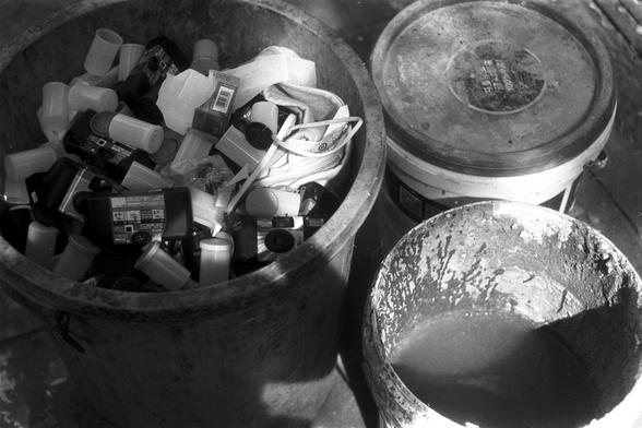 Ilford Pan 100 (FF)

English Alt Text: A black-and-white image showing three large containers. The left container is filled with used disposable cameras, film canisters, and plastic packaging. The middle container is sealed with a lid. The right container is open and contains a liquid substance, possibly water or chemicals, with residue on its inner walls. The scene appears to document the disposal or recycling of analog photography materials.

中文替代文字：
这是一张黑白图像，展示了三个大型容器。左侧容器中装有使用过的一次性相机、胶卷罐和塑料…