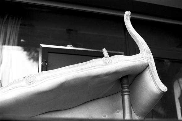 Ilford Pan 100 (FF)

English Alt Text: A black-and-white photo of an upside-down upholstered chair with ornate wooden carvings. The chair is placed in front of a reflective glass surface, possibly a window or door, with curtains visible behind. The underside reveals detailed craftsmanship in the wood and textured fabric. The unusual perspective and contrast between classic furniture and modern glass create a visually intriguing composition.

中文替代文字： 一张黑白照片，画面是一把倒置的软垫椅子，椅子有精美的木雕装饰。它放置在一个反光玻璃表面前，…