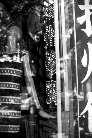 Ilford Pan 100 (FF)

English Alt Text: A black-and-white storefront window scene featuring a mannequin dressed in a patterned outfit. Reflections of trees and surroundings overlay the glass, creating a layered visual effect. Vertical illuminated signs with Chinese characters. Larger Chinese characters are partially visible on the right. The photo blends commercial display with urban reflections, offering depth and cultural texture.

中文替代文字： 一张黑白照片，展示橱窗内的模特，身穿图案服饰。玻璃表面映出树木和周围环境的倒影，形成多层次的视觉效果。垂直的…