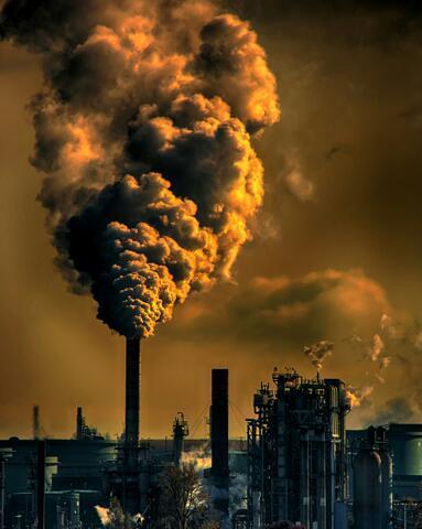 A stock photo of a manufacturing plant with smoke or steam rising into the sky under a dark yellow filter.