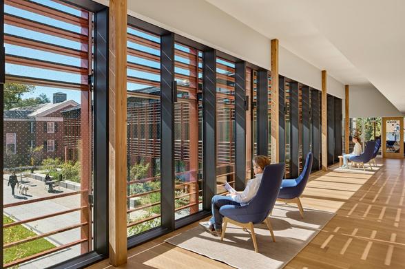 People sitting in a sunny hallway of the Living Village looking out the windows.