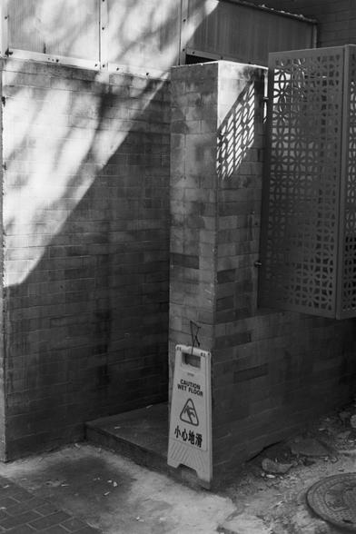 Ilford Pan 100 (FF)

English Alt Text: A corner of a brick building with a textured metal screen on the right side. A yellow “Caution Wet Floor” sign with English and Chinese text stands near the entrance to a small alcove. Shadows from nearby trees cast patterns on the wall. The ground is uneven, with debris and a manhole cover visible. The scene is outdoors in an urban setting, suggesting recent cleaning or rain.

中文替代文字：
一栋砖砌建筑的角落，右侧有一个带纹理的金属屏障。地面上放着一个黄色的“Caution Wet Floor（小心地滑）”警示牌，靠近一个小通道入…
