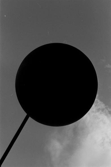 Ilford Pan 100 (FF)

English Alt Text:
A large, dark circular object is silhouetted against a partly cloudy sky in this black-and-white photo. Mounted on a pole, the object resembles a street sign or disc. The photo is taken from a low angle, making the circle appear dominant in the frame. The sky transitions from darker to lighter tones, adding depth. The stark contrast between the object and the sky creates a bold, minimalist composition.
中文替代文本：  
这是一张黑白照片，画面中一个大型黑色圆形物体在多云的天空前形成剪影。它安装在一根杆子上，…