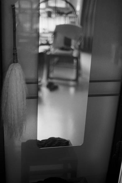Ilford Pan 100 (FF)

English Alt Text:
A black-and-white photo captures a mirror reflecting a room. In the reflection, a chair, a pair of shoes on the floor, and a window with vertical blinds or bars are visible. To the left of the mirror, a hanging object resembling a fly-whisk with soft bristles is seen. The composition uses reflection to create a layered visual effect, blending real and mirrored elements in a quiet, introspective setting.

中文替代文字：
这是一张黑白照片，镜子反射出一个房间的景象。镜中可见一把椅子、地上的一双鞋，以及带有垂直…