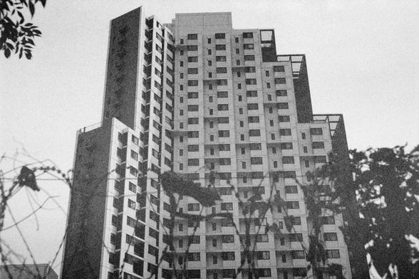 Ilford HP5 Plus 400 (FF)

English Alt Text:  
A black and white image showcases a tall, modern high-rise building with a geometric, staggered design. The facade features numerous windows and balconies, creating a rhythmic pattern. Silhouetted tree branches frame the building in the foreground, adding a natural contrast to the urban structure. The photo emphasizes architectural complexity and the interplay between nature and city life.
中文替代文字：  
这是一张黑白照片，展示了一栋高耸的现代高层建筑，设计上采用几何错落结构。外墙布满窗户和阳台，形成有节…