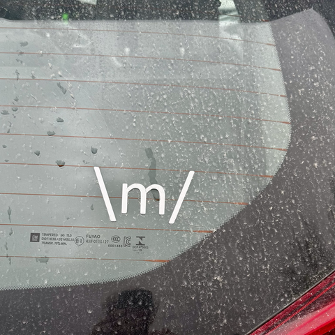iPhone photo of the raindrop covered back window of my car w/ a backslash lower case m forward slash bumper sticker