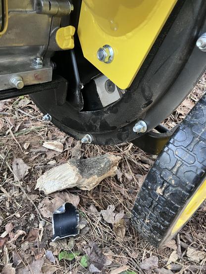 A close-up of the bottom portion of the chipper, showing a damaged area where the blade has sheared off 3 square inches of metal. The metal piece lays on the ground alongside the piece of wood that jammed it.