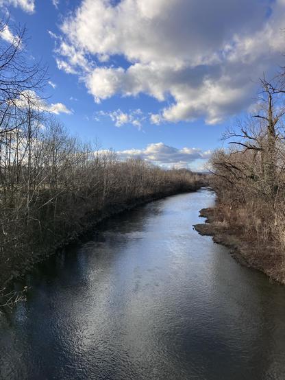 The Roanoke River winds amidst the bare trees, under a partially cloudy blue sky.