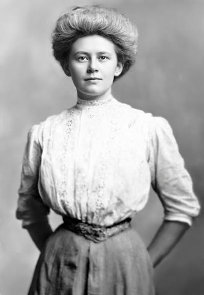 Photo of my grandmother, Lena, around 1910. A young white woman looking straight at the camera, hands behind her back. She’s wearing a 3/4 sleeve white blouse with vertical strips of lace down the front, and a light-colored skirt cinched tightly at her waist. Her hair is neat,y coiffed in a sort of bouffant updo style.
The photo has been repaired using photoshop’s AI nano banana pro tool.