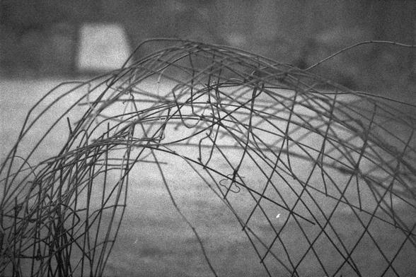 Ilford HP5 Plus 400 (FF)

English Alt Text: A dome-like wire sculpture composed of thin, overlapping wires forms a chaotic yet geometric pattern. The black-and-white image emphasizes shadows cast on the ground, creating a layered visual effect. The background is blurred, drawing focus to the intricate wirework. The abstract composition evokes themes of fragility, complexity, and spatial tension.

中文替代文本： 一个穹顶状的铁丝结构由细小交错的线条构成，呈现出混乱而几何的图案。黑白照片突出地面上的阴影，营造出层次感。背景模糊，使观者聚焦于精致的线条构造。抽象构图传达出脆弱、复杂与空间张力的主…