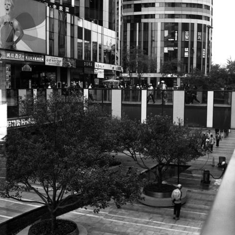 Lucky SHD 400 (6x6)

English Alt Text: A black-and-white image of a bustling urban plaza. Tall buildings with reflective glass facades and Chinese signage surround the area. A large advertisement featuring a person dominates one building. Trees are planted in circular planters along paved walkways. An elevated pedestrian bridge connects parts of the complex, with people walking across it. The scene blends architecture, nature, and human activity in a vibrant commercial setting.

中文替代文本：
这是一张黑白照…